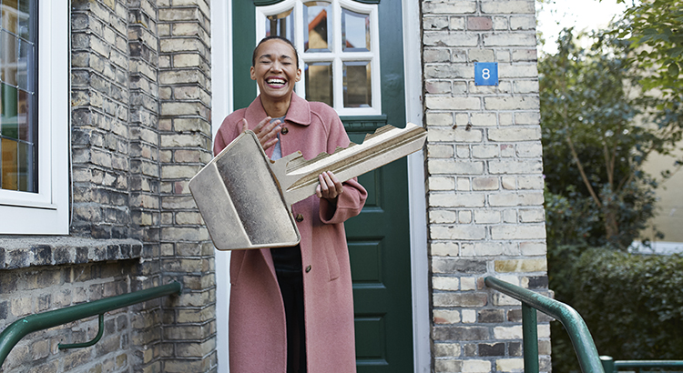 Cheerful young woman holding large key outside new house